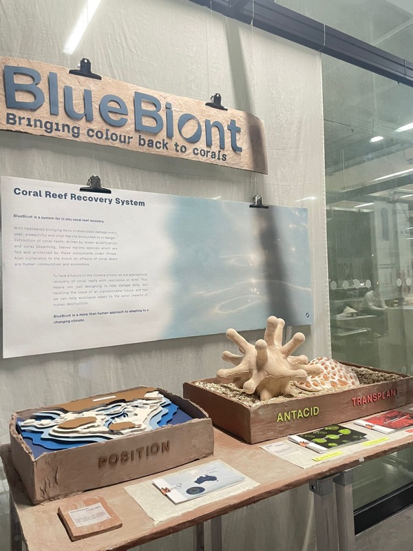 Exhibition table with the Blue Biont sign, a text panel, a layered model of the reef and the prototype
