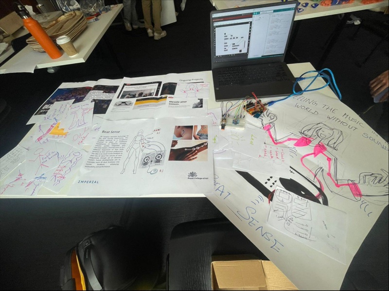 Table covered with printed research, sketches, a laptop and the Arduino prototype